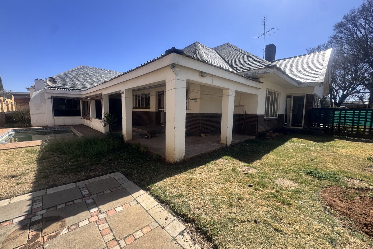 Rear view of the property featuring a covered patio, swimming pool, and established garden area with a tiled roof and brick exterior finish.