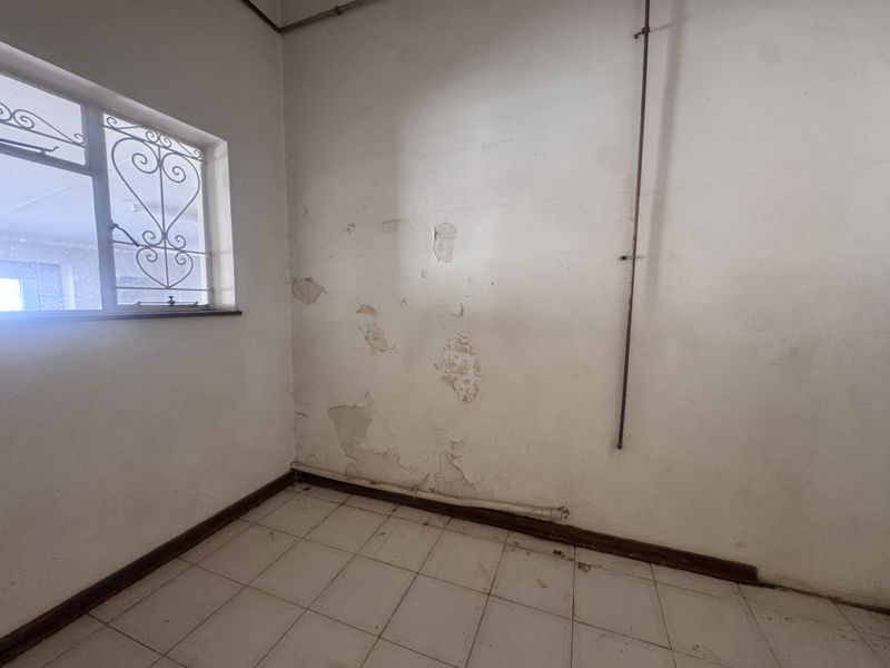 A vacant utility space featuring tiled flooring, security bars on the window, and visible wall surface deterioration requiring maintenance and repair.