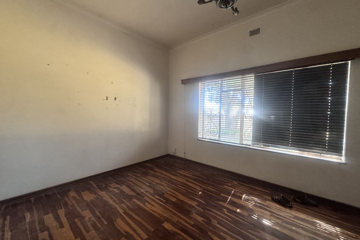 An empty bedroom featuring timber flooring, a ceiling fan, and venetian blinds, requiring minor wall repairs and floor refinishing.