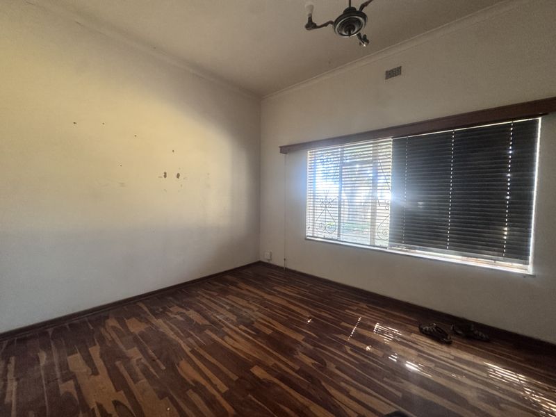 An empty bedroom featuring timber flooring, a ceiling fan, and venetian blinds, requiring minor wall repairs and floor refinishing.