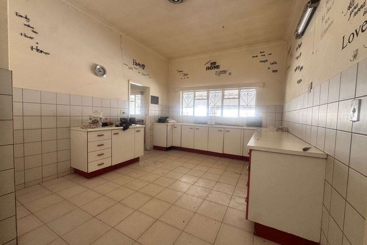 A spacious, empty kitchen featuring tiled flooring, built-in cabinetry with tiled splashbacks, and security bars on the windows, ready for renovation.