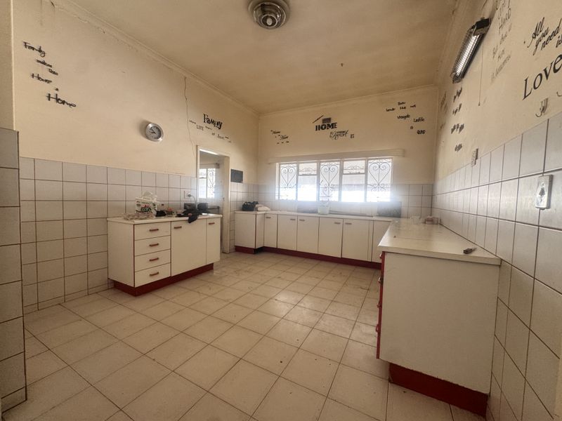 A spacious, empty kitchen featuring tiled flooring, built-in cabinetry with tiled splashbacks, and security bars on the windows, ready for renovation.