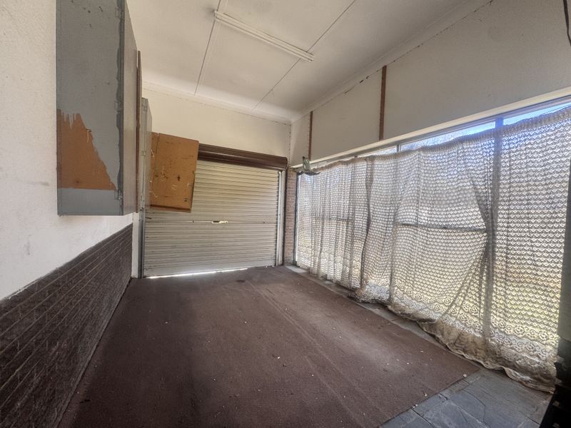 A spacious garage featuring a roller shutter door, built-in storage cabinetry, and large windows, offering potential for renovation or workshop conversion.