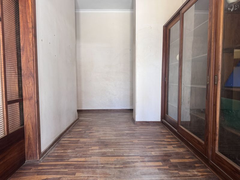 A vacant hallway featuring built-in wooden cabinetry with sliding glass doors and laminate flooring, requiring minor cosmetic updates to refresh the space.