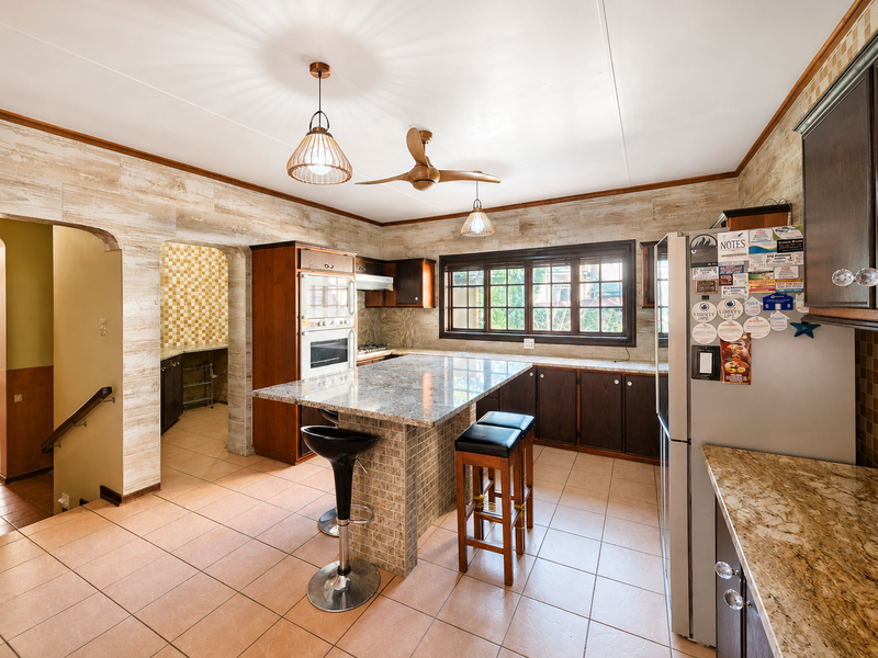 Spacious kitchen featuring granite countertops, a central island, built-in oven and microwave, tiled flooring, and ample wooden cabinetry with a connected scullery area.