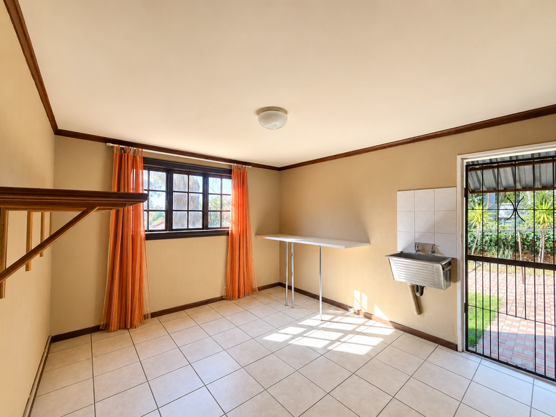 A functional laundry room featuring a stainless steel utility sink, tiled flooring, and direct access to the outdoor area through a security gate.