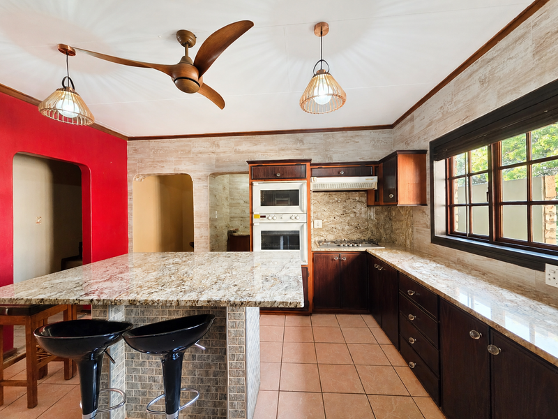 Spacious kitchen featuring granite countertops, built-in oven and microwave, gas hob, extractor fan, and ample wooden cabinetry with a central island.