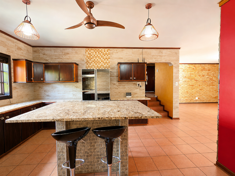 Spacious kitchen featuring granite countertops, built-in cabinetry, and a central island, flowing into an adjacent living area with exposed brick walls.