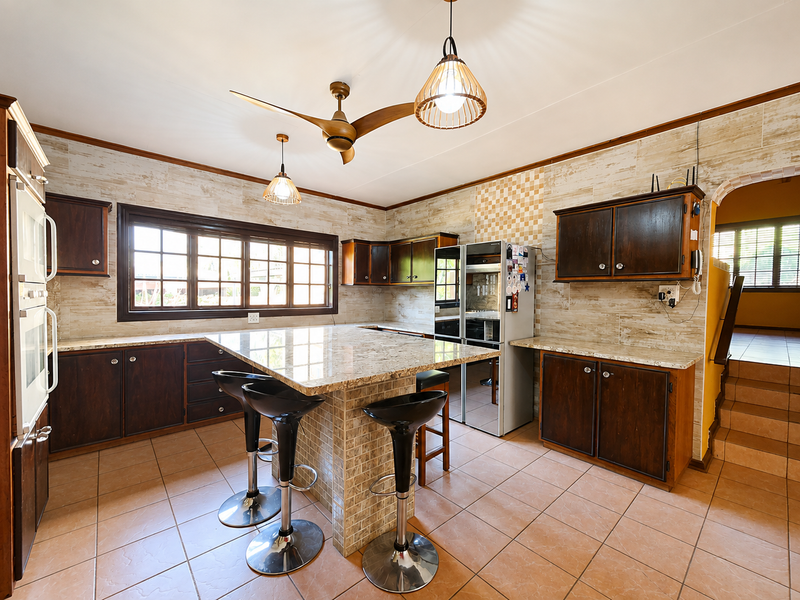 Spacious kitchen featuring granite countertops, dark wood cabinetry, tiled backsplash, and a central island with breakfast bar seating.