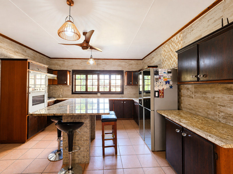 Spacious kitchen featuring dark wood cabinetry, granite countertops, a central island with breakfast bar seating, and tiled finishes throughout.