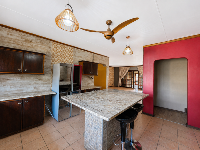Kitchen featuring a large granite island, tiled splashback, built-in cabinetry, and pendant lighting, flowing into an adjacent living area.
