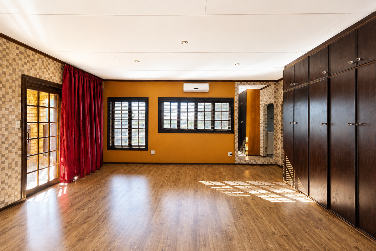 Spacious bedroom featuring extensive built-in dark wood cabinetry, laminate flooring, air conditioning, and direct access to an outdoor area through a timber-framed glass door.
