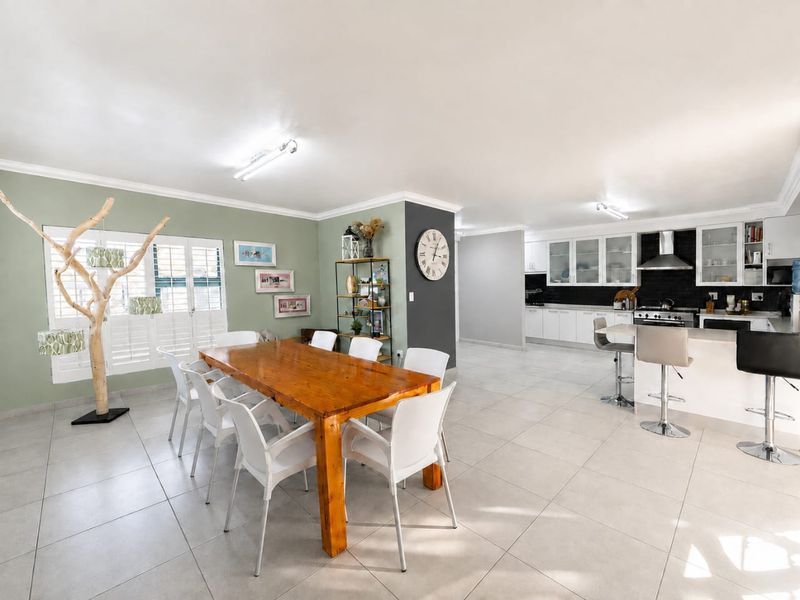 Spacious open-plan living and dining area featuring tiled floors, plantation shutters, and a modern kitchen with a central island and built-in appliances.