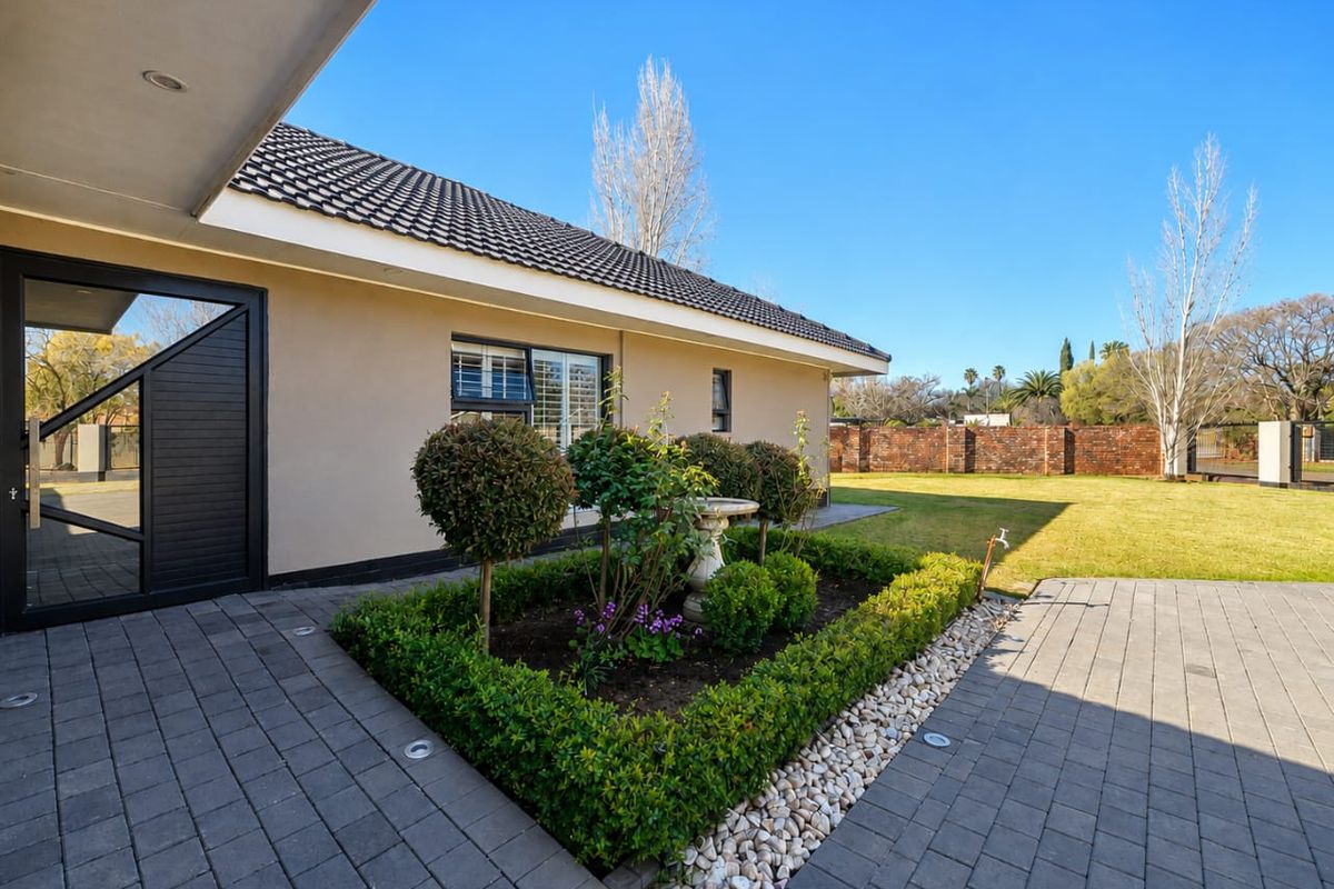 A well-maintained rear exterior featuring a paved patio, landscaped garden beds, and a brick boundary wall under a clear blue sky.