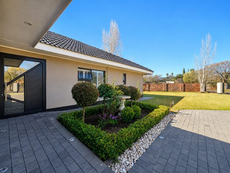 A well-maintained rear exterior featuring a paved patio, landscaped garden beds, and a brick boundary wall under a clear blue sky.