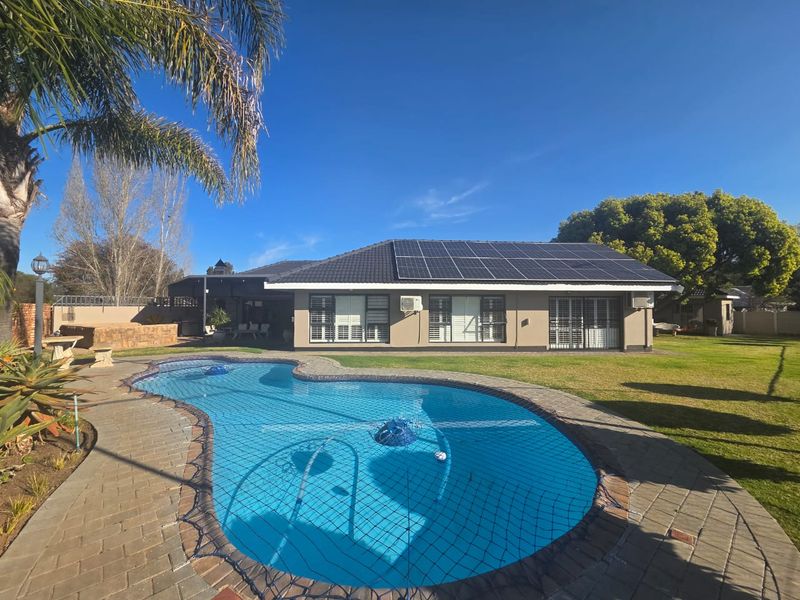 Rear view of the property featuring a swimming pool with safety net, solar panels on the roof, and a well-maintained garden area.