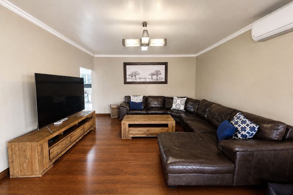 A well-maintained living room featuring warm-toned laminate flooring, crown molding, and a wall-mounted split-system air conditioner.