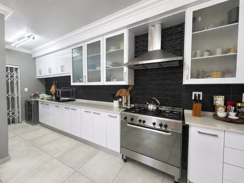 Modern kitchen featuring white cabinetry, stone countertops, a black tiled backsplash, and a stainless steel gas stove with an extractor fan.