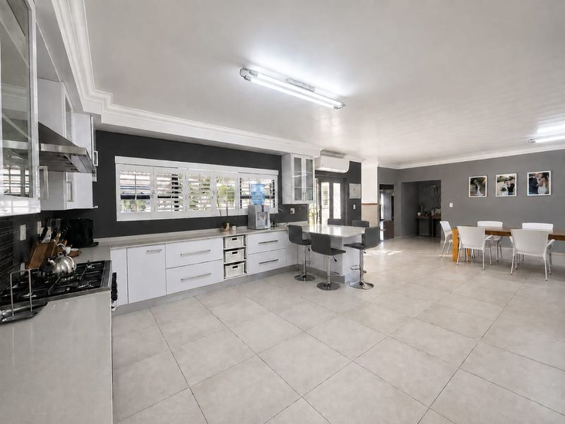 Spacious open-plan kitchen and dining area featuring modern white cabinetry, a central island, gas hob, and large format floor tiles.