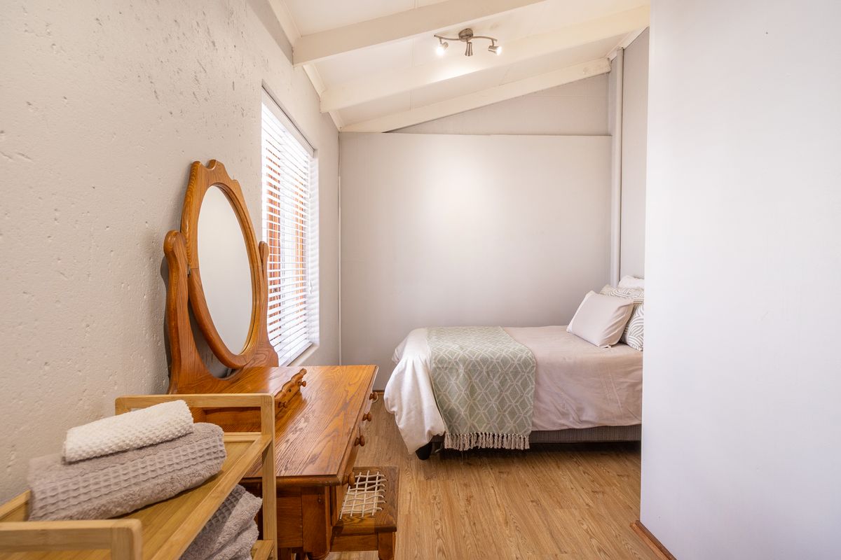 A cozy bedroom featuring exposed rafters, laminate flooring, and natural light through venetian blinds.