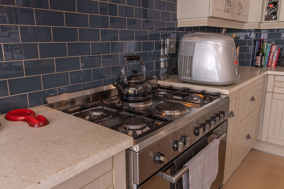 A well-maintained kitchen featuring a stainless steel gas range, stone countertops, and dark blue subway tile backsplash with classic shaker-style cabinetry.