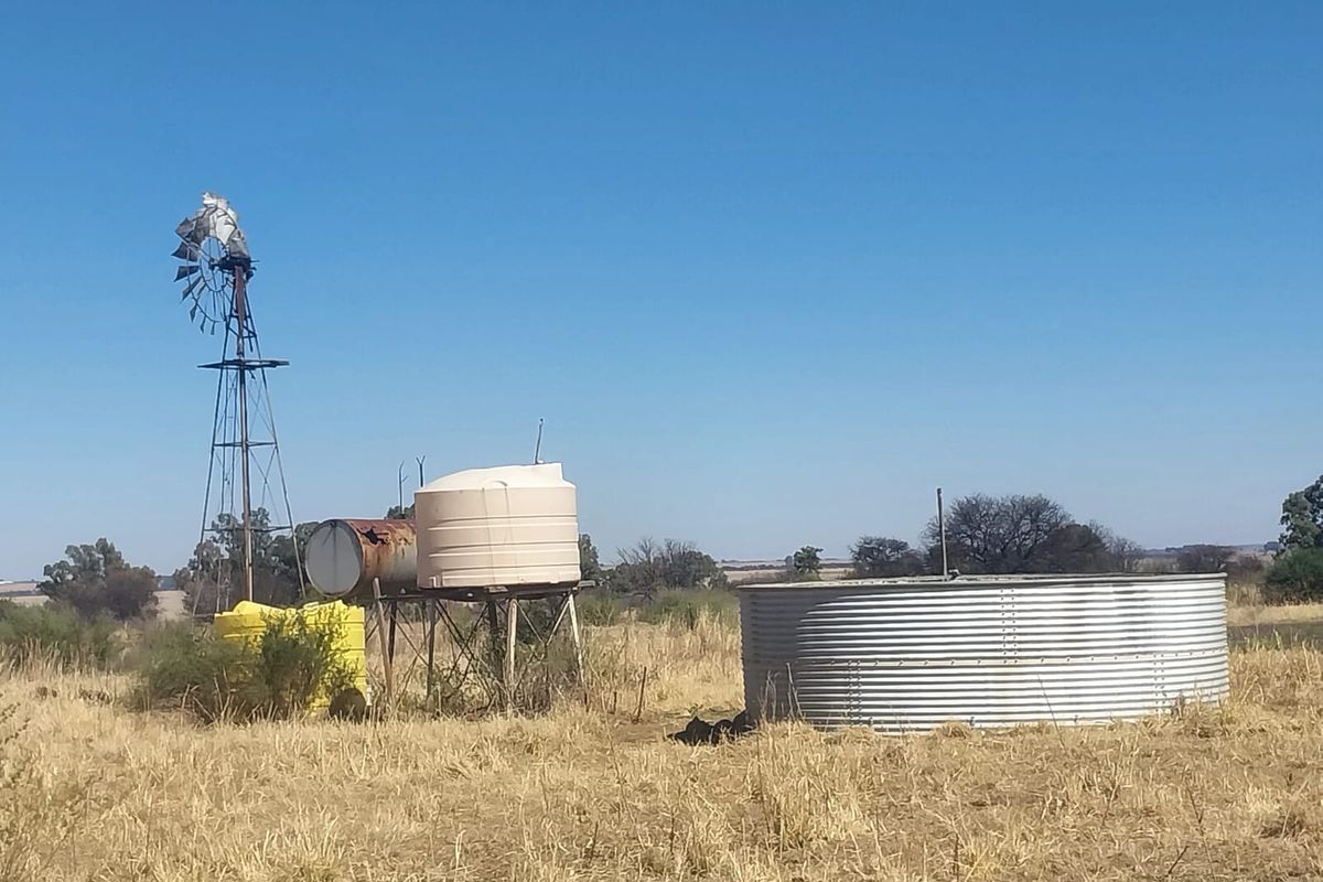 Farm utility area featuring a windmill, plastic water storage tanks, and a large corrugated steel reservoir for agricultural water management.