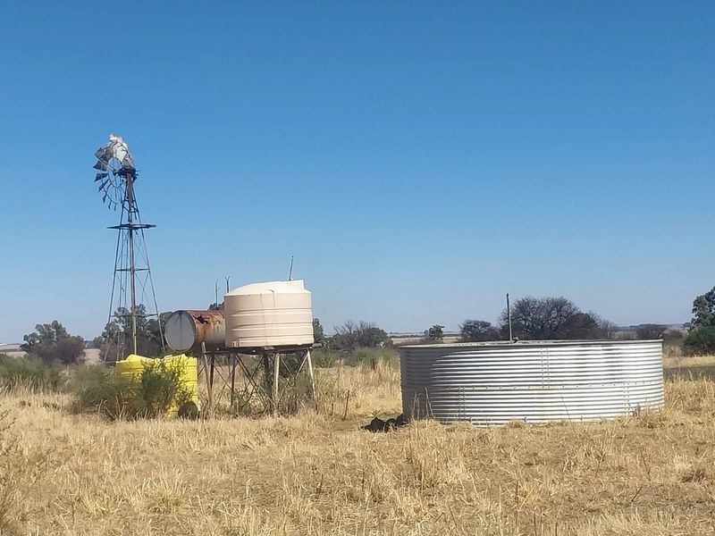 Farm utility area featuring a windmill, plastic water storage tanks, and a large corrugated steel reservoir for agricultural water management.