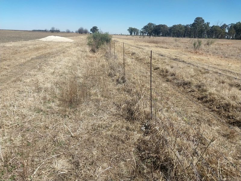 A view of the expansive farm land featuring a simple barbed wire fence boundary line.