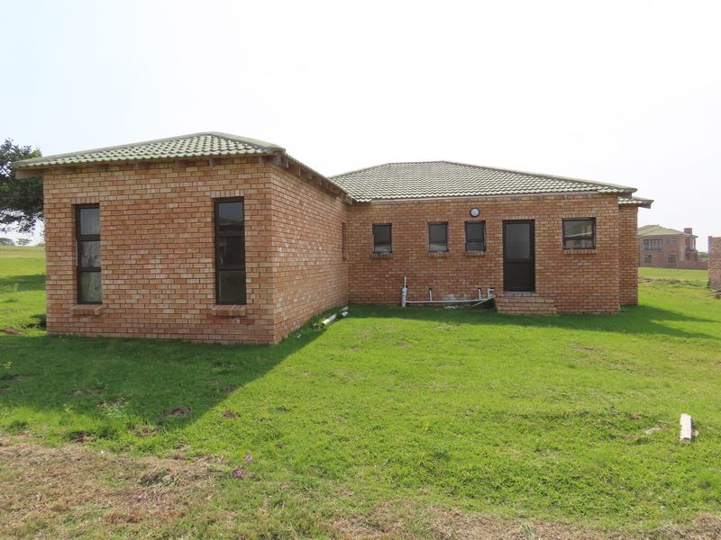 Rear view of a face brick house featuring a tiled roof and aluminium window frames, set on a grassed plot.