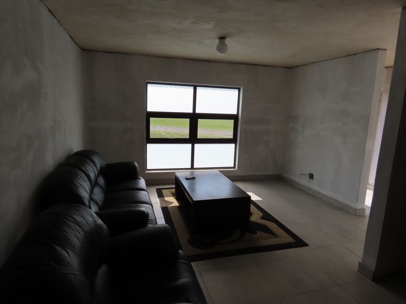 A living room space featuring tiled flooring and an aluminium window, currently requiring final wall finishing and painting to complete the interior.