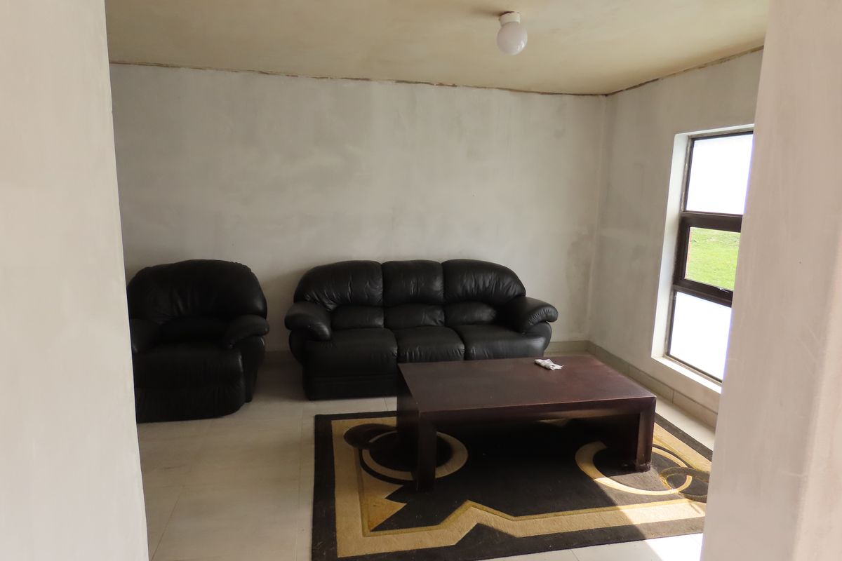 A living room space featuring tiled flooring and an aluminium window, currently requiring finishing touches to the walls and ceiling.