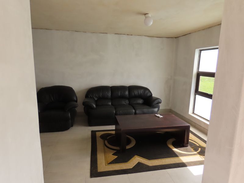 A living room space featuring tiled flooring and an aluminium window, currently requiring finishing touches to the walls and ceiling.