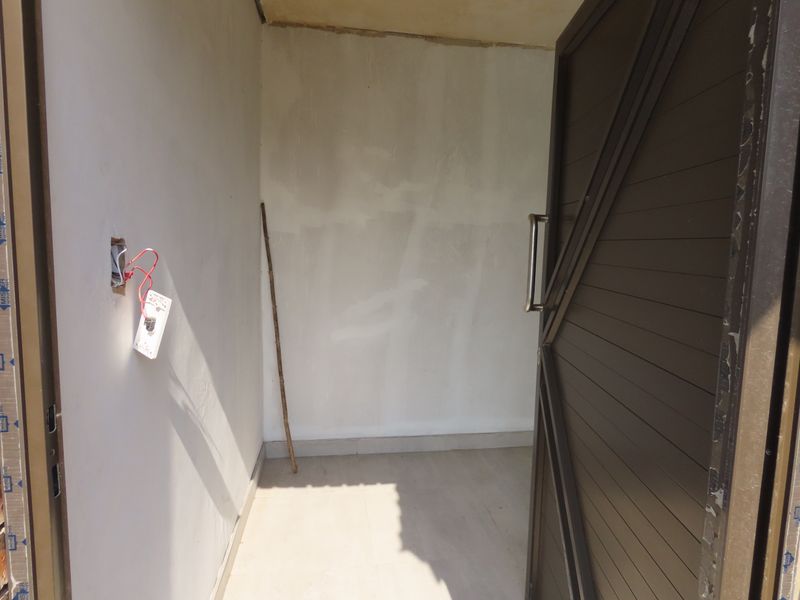 An unfinished entryway featuring tiled flooring and an aluminium door, currently requiring electrical finishing and wall surface completion.