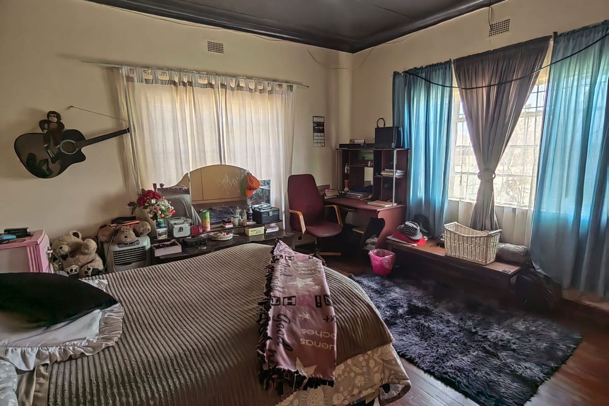 A bedroom featuring hardwood flooring, a ceiling fan, and dual windows. The room requires cosmetic updates to the ceiling and wall finishes.