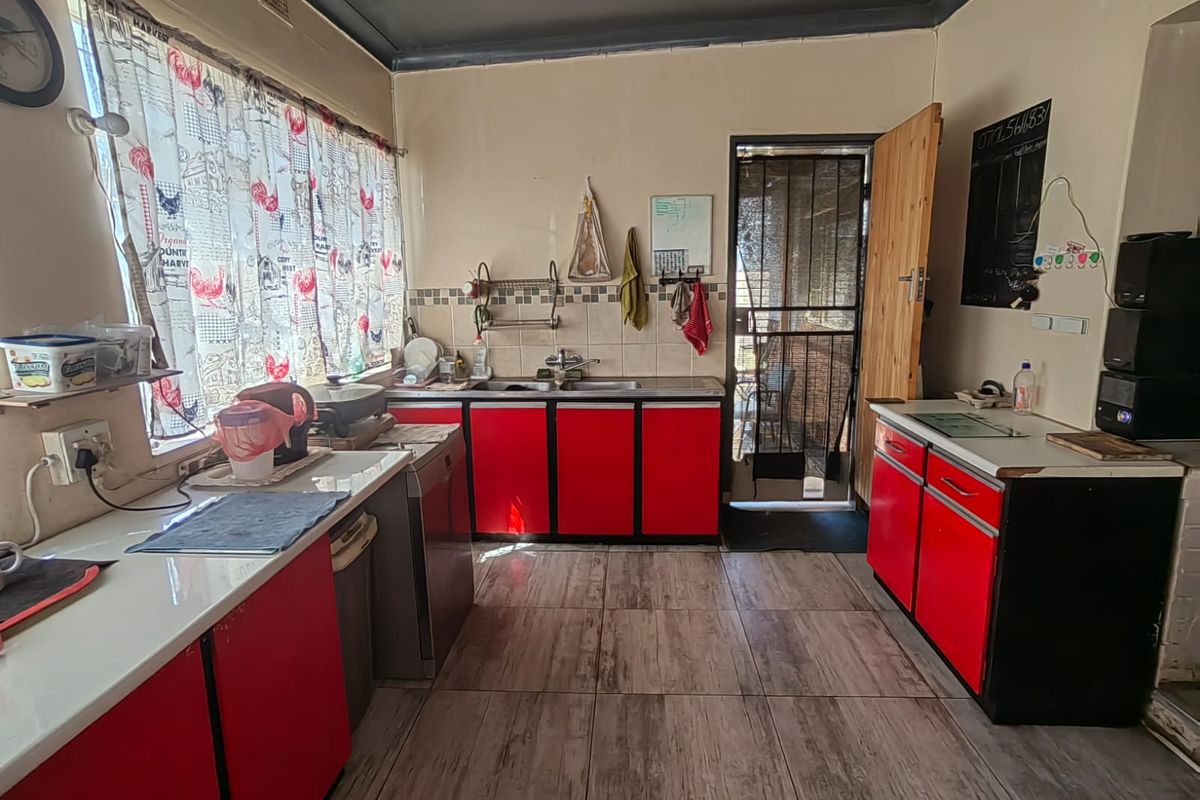 A functional kitchen featuring red cabinetry, a double sink, tiled backsplash, and direct access to an exterior security gate.