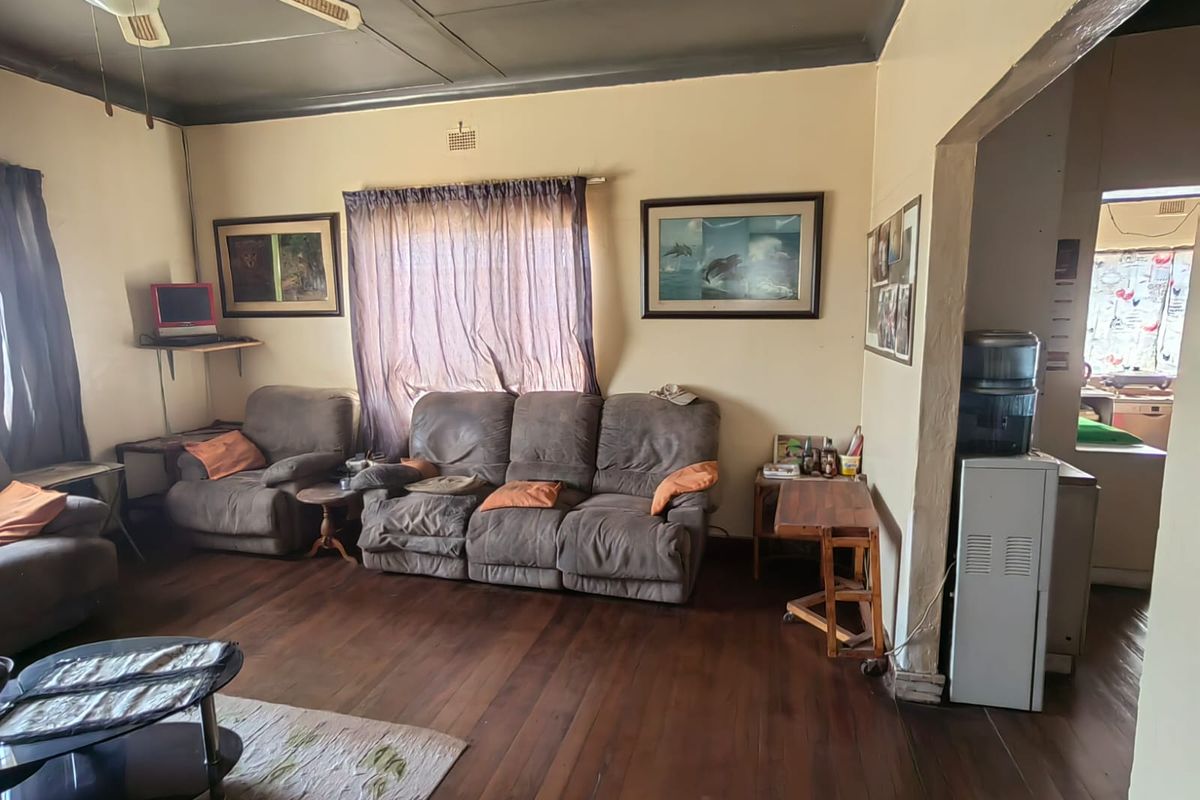 A living room featuring timber flooring and a ceiling fan, with an open-plan transition leading into the adjacent kitchen area.