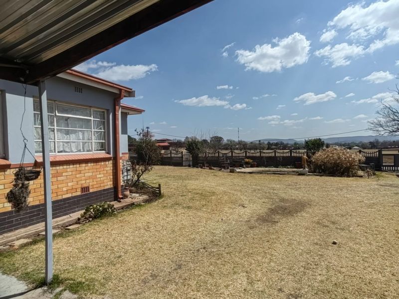 A view of the rear garden and exterior facade of the house, featuring a brick and plaster finish with a corrugated metal roof.