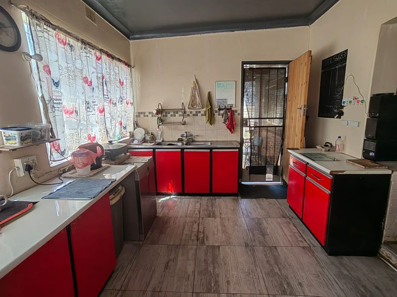 A functional kitchen featuring red cabinetry, a double sink, tiled backsplash, and direct access to an exterior security gate.