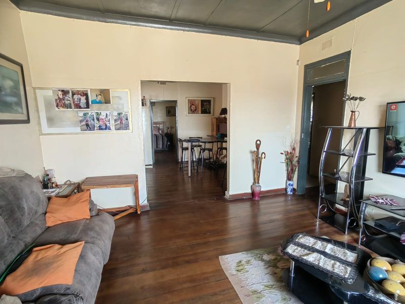 A living room featuring original hardwood flooring and a timber ceiling, with an open archway leading to an adjacent dining area.