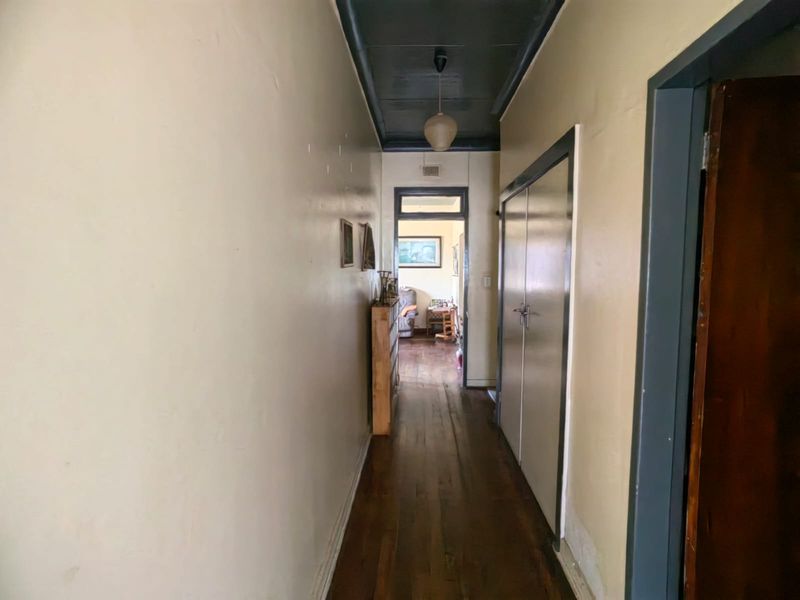 A narrow residential hallway featuring dark hardwood flooring, built-in storage cupboards, and a contrasting dark-painted ceiling.