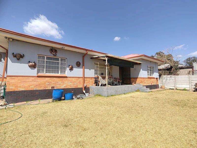 Rear view of a single-story house featuring a brick and plaster facade, a concrete patio area, and a metal roof.
