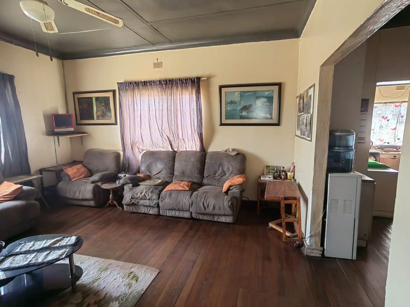A living room featuring timber flooring and a ceiling fan, with an open-plan transition leading into the adjacent kitchen area.