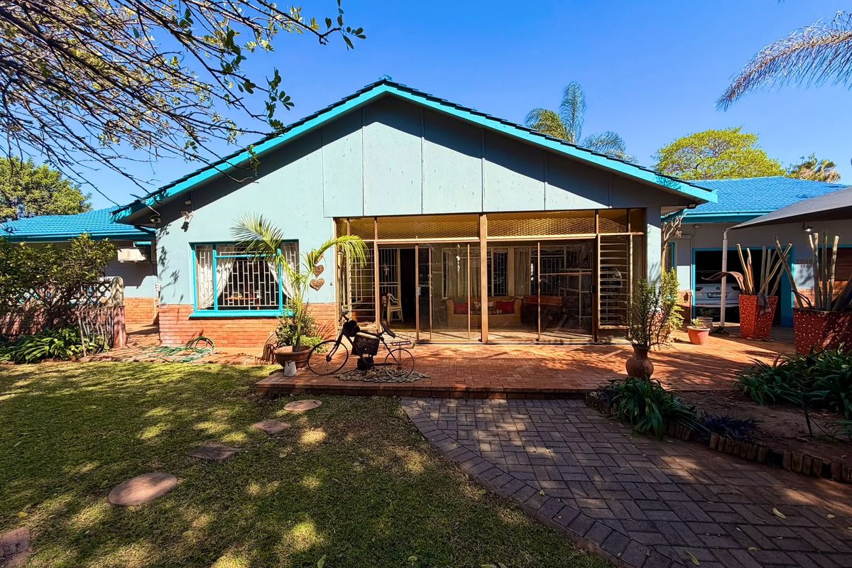 Rear view of the house featuring a brick paved patio, sliding glass doors with security bars, and a landscaped garden area.