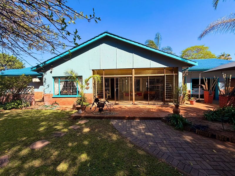 Rear view of the house featuring a brick paved patio, sliding glass doors with security bars, and a landscaped garden area.