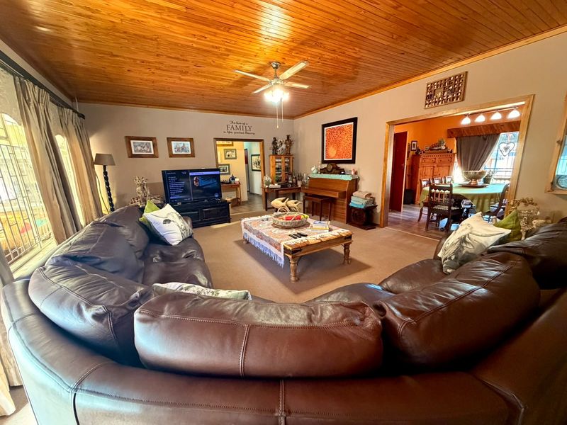 Spacious living room featuring a warm timber tongue and groove ceiling, ceiling fan, and carpeted flooring, with an open flow to the adjacent dining area.