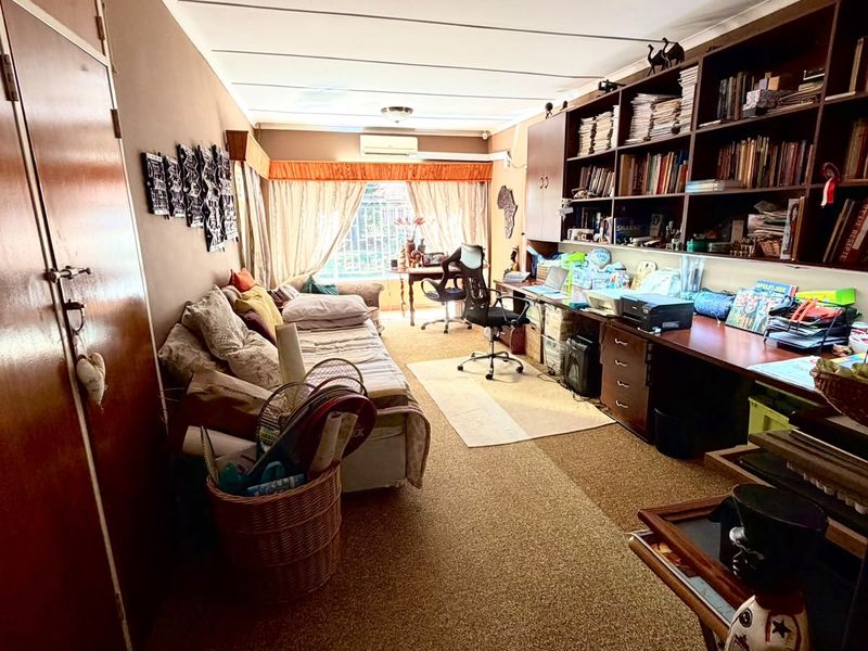 A multi-purpose living area featuring extensive built-in shelving and desk space, with a split-system air conditioner and carpeted flooring.