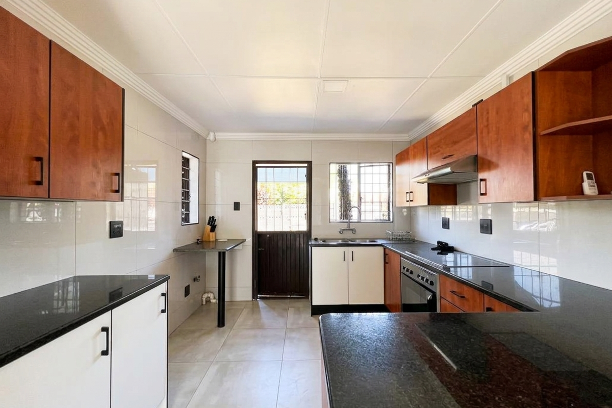 A clean, functional kitchen featuring dark granite countertops, wood-finish cabinetry, built-in oven, extractor fan, and tiled finishes with direct access to the exterior.