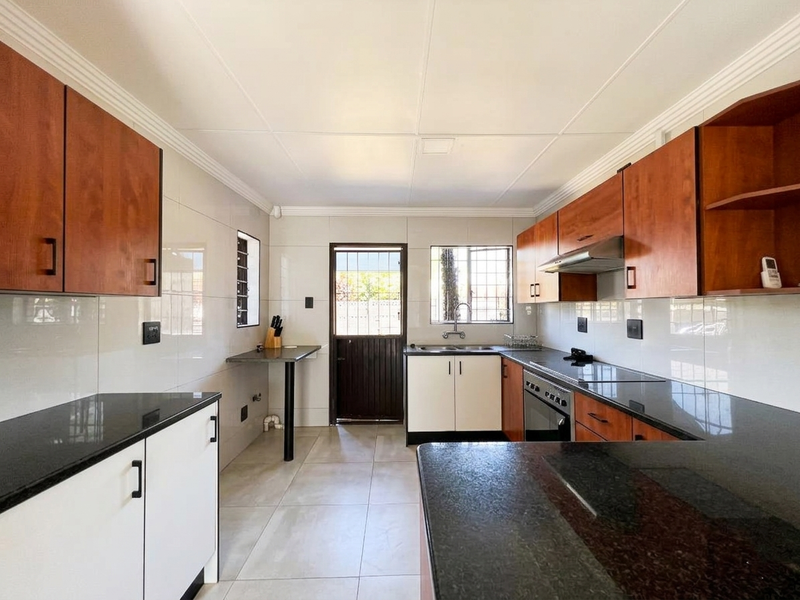 A clean, functional kitchen featuring dark granite countertops, wood-finish cabinetry, built-in oven, extractor fan, and tiled finishes with direct access to the exterior.