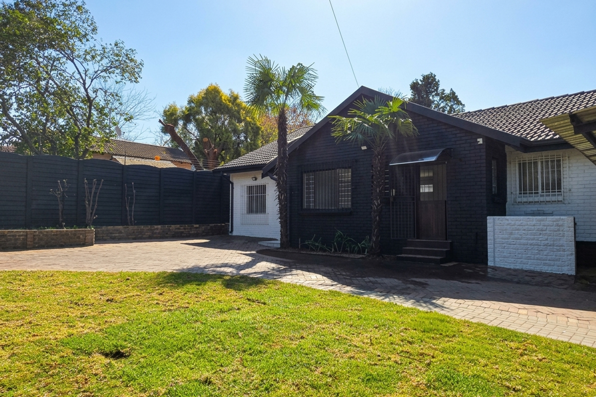 Rear exterior view of the property featuring a paved driveway, landscaped lawn, and a modern painted brick facade with security bars.