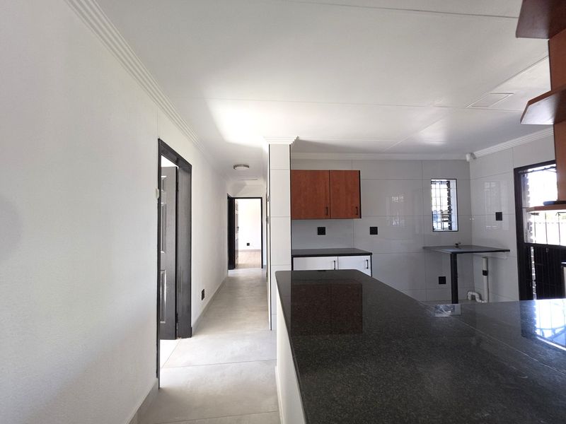 Open plan kitchen area featuring granite countertops, built-in cabinetry, and neutral tiled flooring, leading into a hallway with access to other rooms.